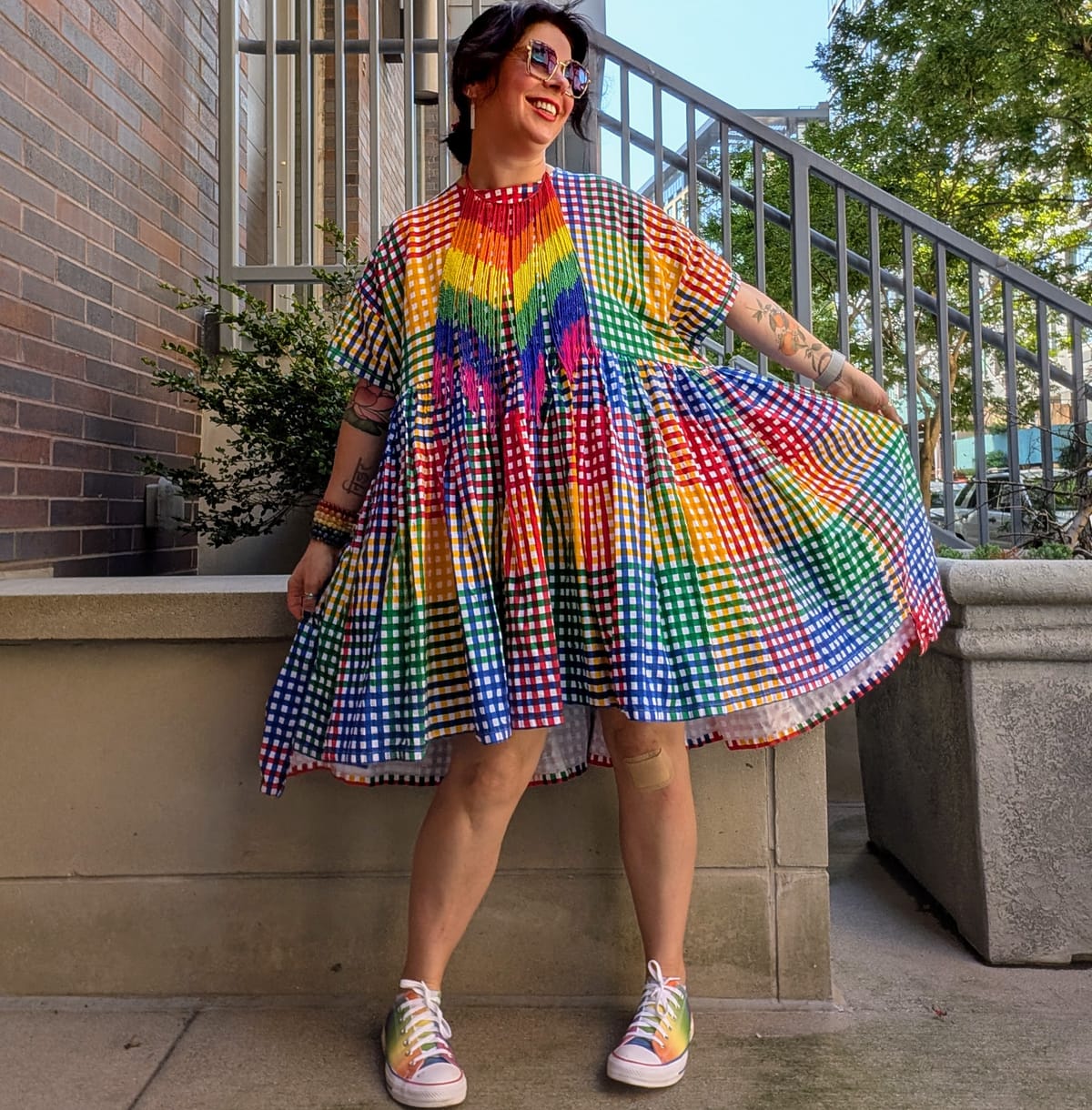 I am standing outside in a rainbow plaid dress with rainbow converse shoes and a rainbow bib necklace