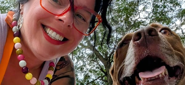 I am smiling at the camera with orange glasses and a big, fun, beaded necklace on. My dog is next to me, also smiling.